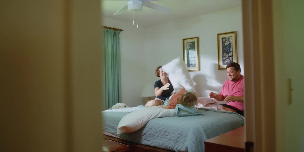 A man and woman have a pillow fight with their young boy