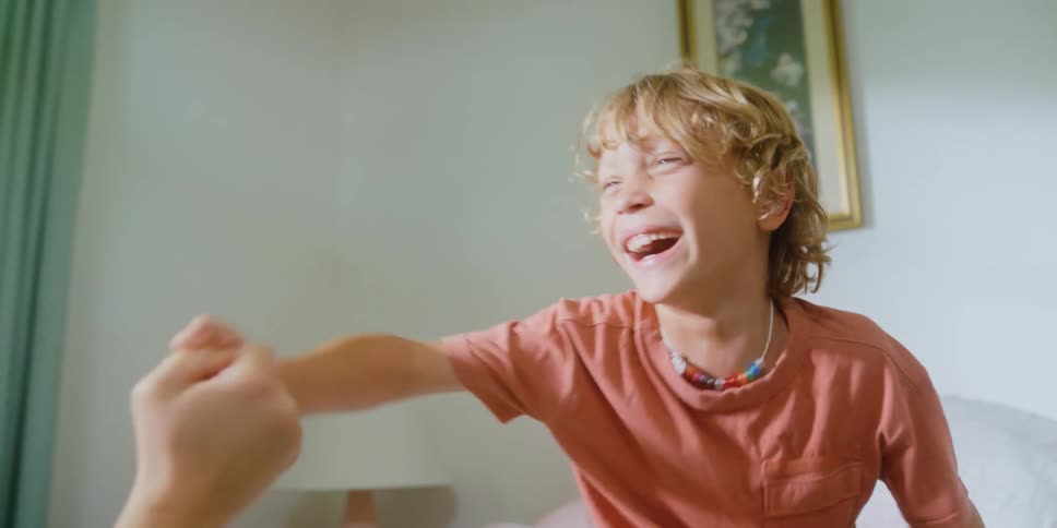 Young blonde boy playing with his mother over the bed at home
