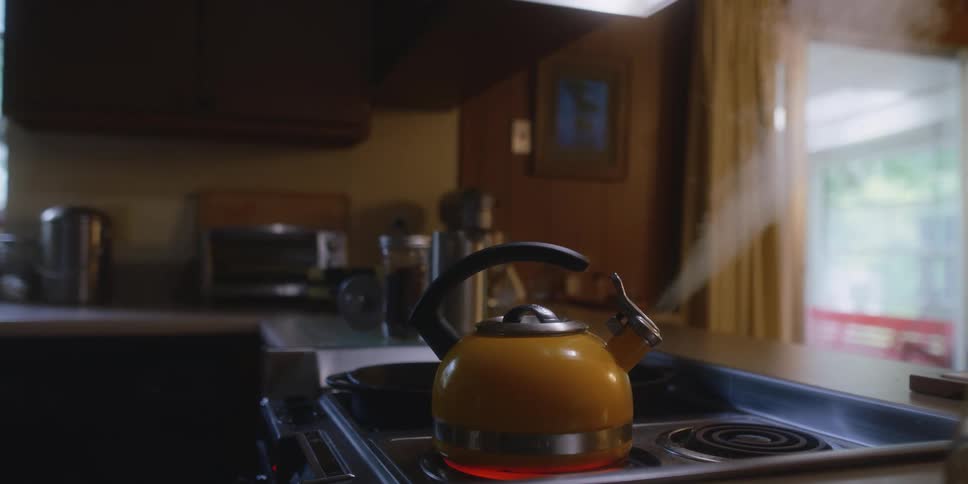Steam shoots out of the tea kettle that is on the burner of a stove