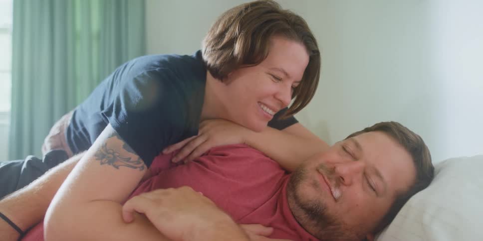 Wife with tattoo and dark t shirt kisses husband and caresses his chest in the bedroom