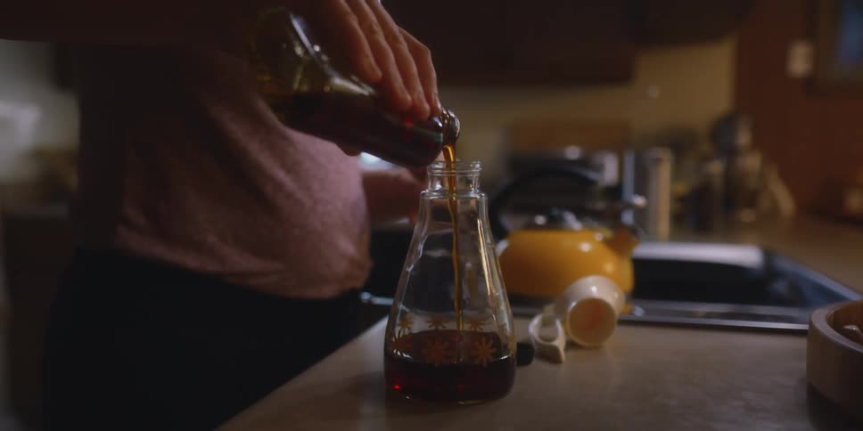 A woman pours dark syrup into a container from a bottle