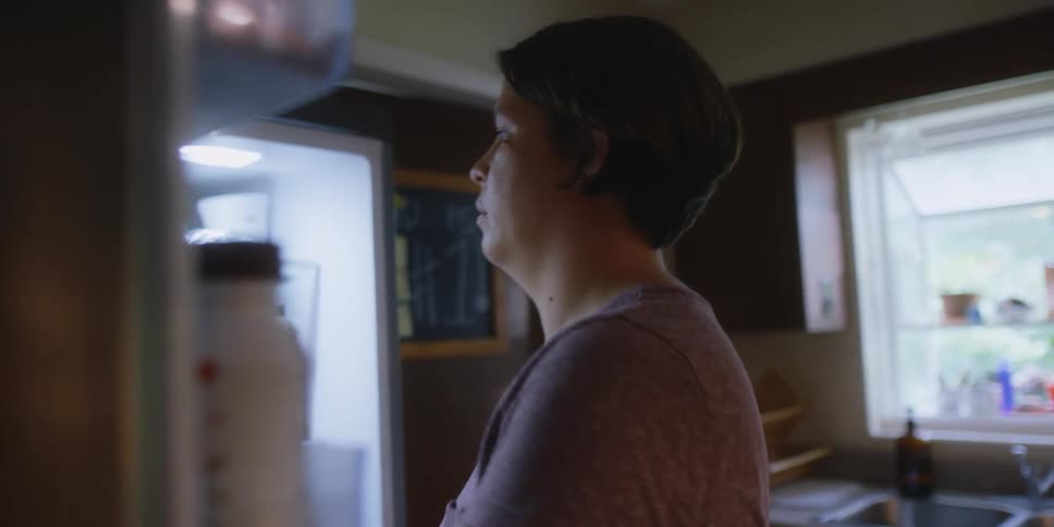A woman is getting food from a fridge in her kitchen