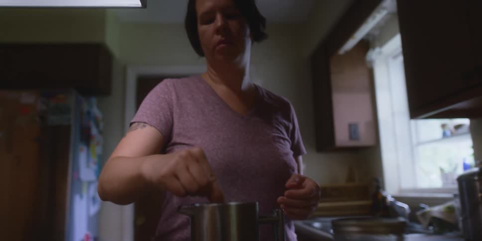 A woman in a kitchen mixing a drink in a mug with a refrigerator and a door in the background