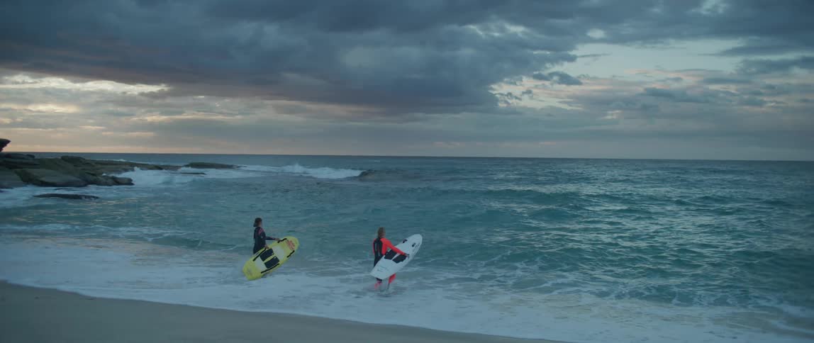 Two people are surfing in the ocean at dusk