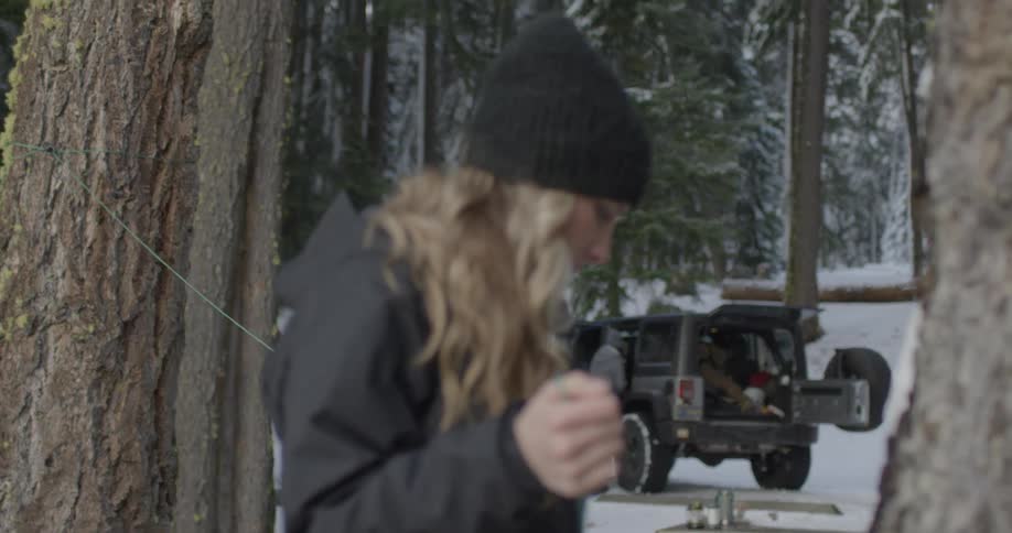 A woman strings green wire in between trees outside in the winter