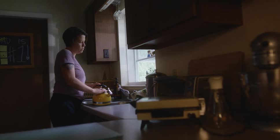A woman stands at a kitchen sink and fills a tea pot with water