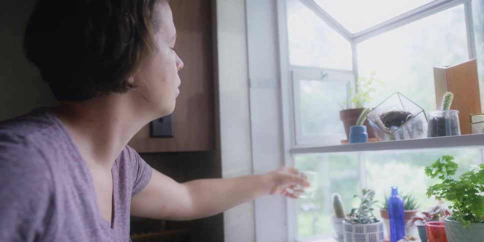 Woman waters her plants that are on shelves in a window