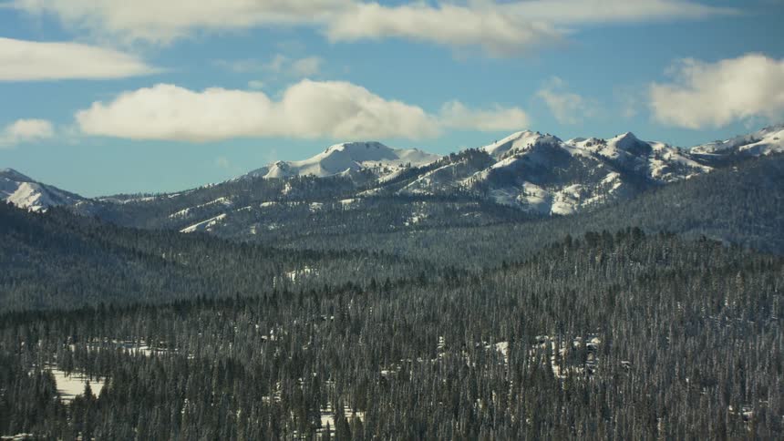 A mountainous countryside covered in snow and forest under a clear blue sky