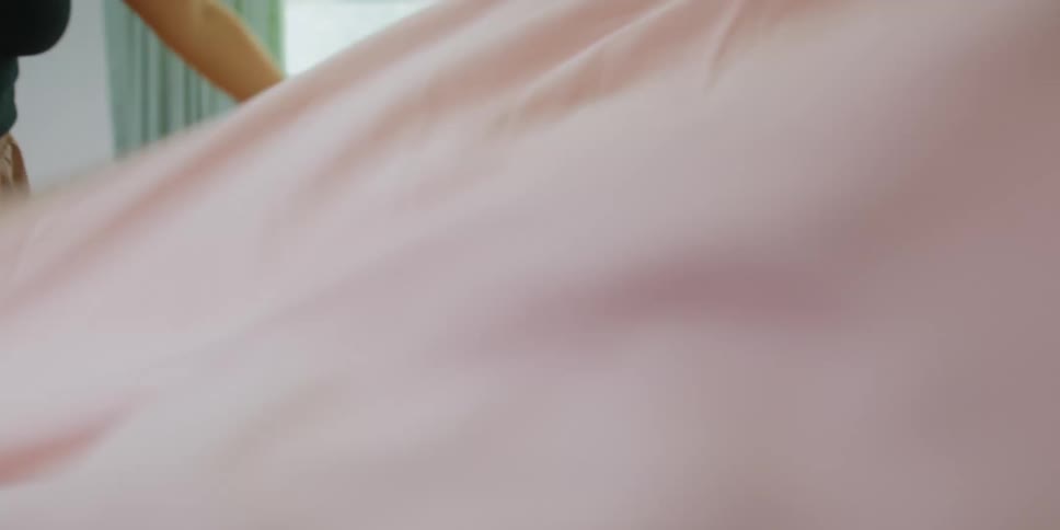 Toddlers laying in bed excitedly laughing while their mother plays with the bed sheets
