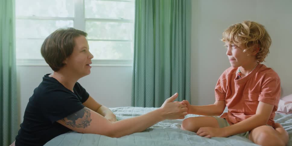 A woman and young boy play thumb wrestling in a bedroom