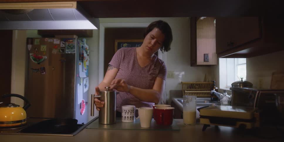 Woman serves milk and coffee on a mug over the kitchen counter at home