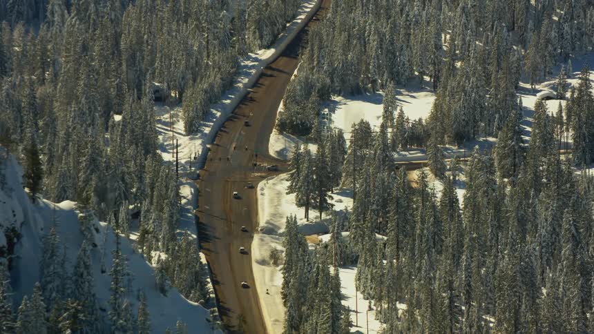 Road with light traffic surrounded by snow covered forests and mountains