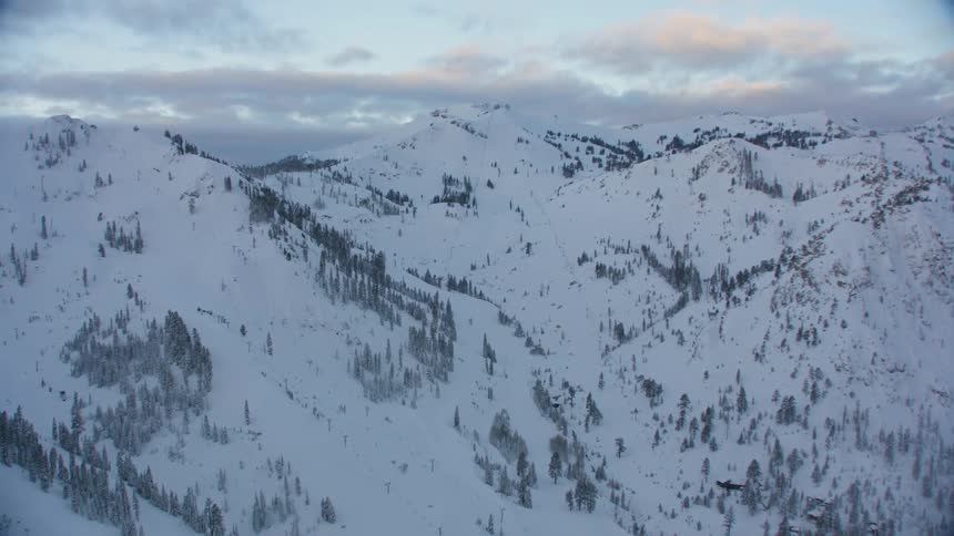 A mountain range with trees covered in snow with the sky and clouds in the background
