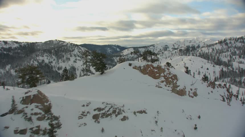 Snow and conifer trees cover mountain slopes and valley under cloudy sky