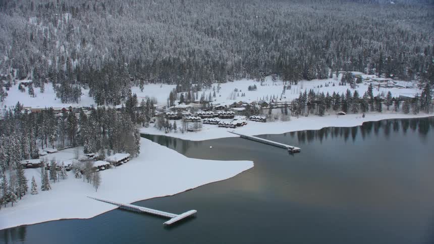 An aerial view of a forest behind the snow covered shore and water