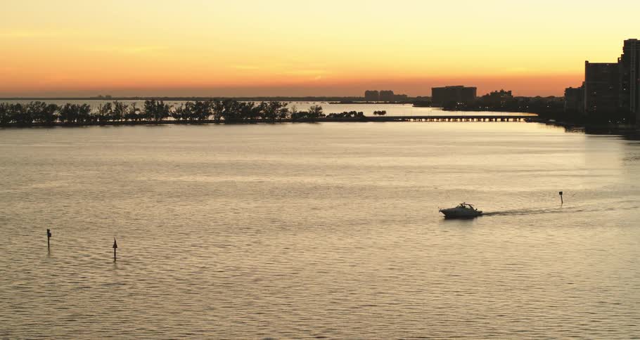 A boat traveling away from a city in the ocean at sunset