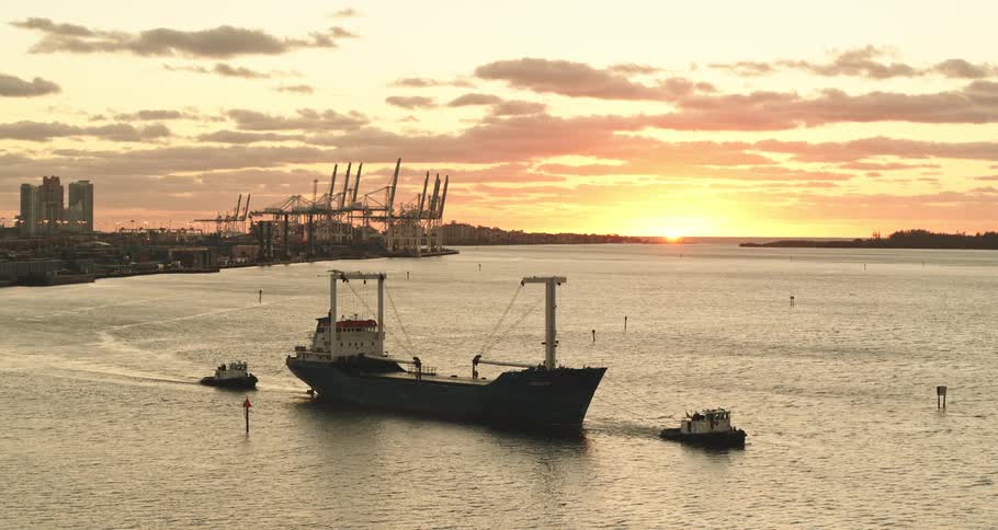 A large boat is towed down a river by two tugboats