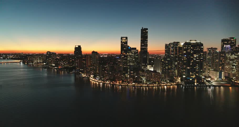 City skyline lights glow and shimmer off the water at sunset
