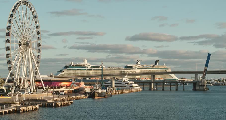 A cruise ship looms in the distance beyond a fairground on the coast during the day