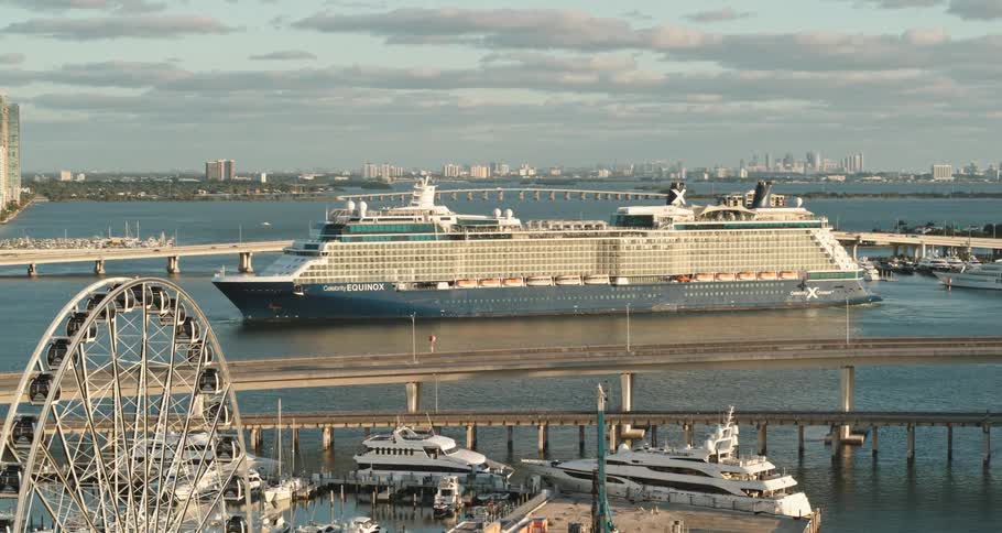 A large cruise ship waits in the ocean between bridges on the coast of a city during the day