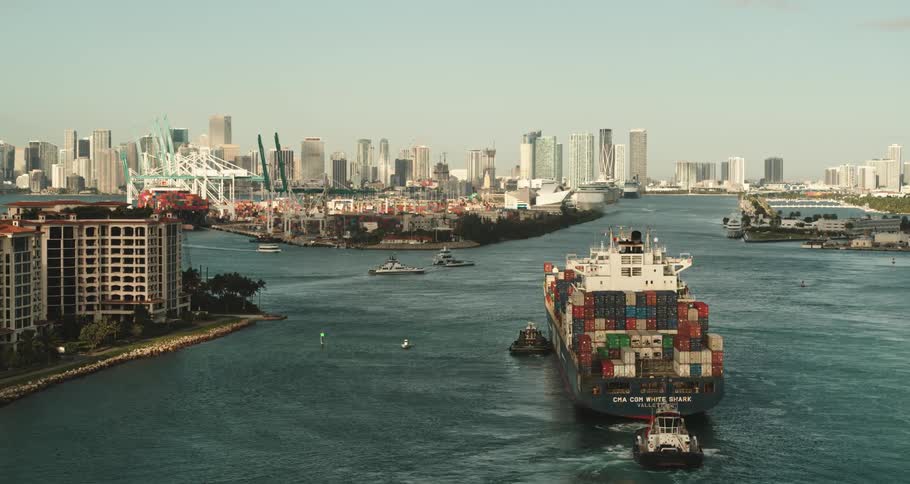 A large ship full of shipping containers moves slowly in a river marina