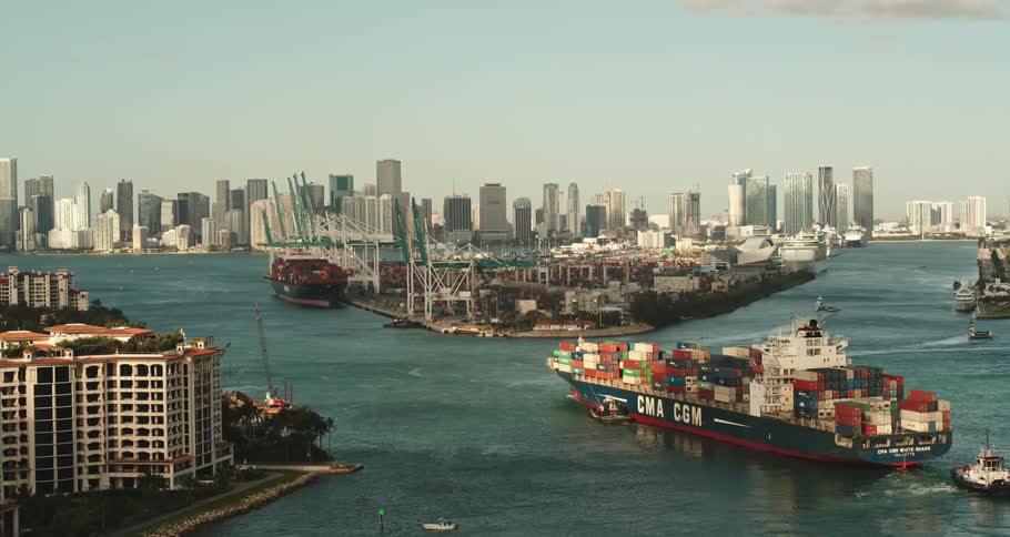 A ship loaded with shipping containers floats in the river that flows through a city