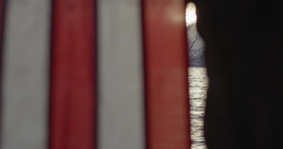 Close up of a flag blowing in the breeze by a window and a view of a lake