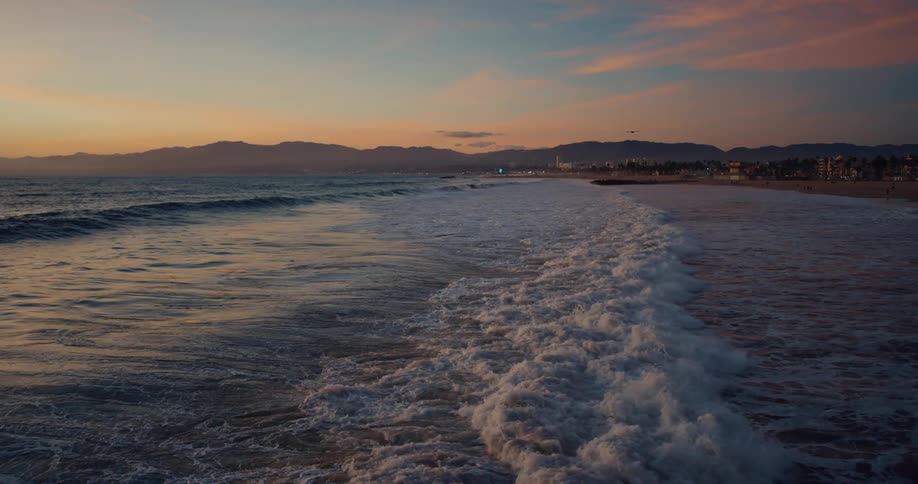 Ocean waves crash against the long beach at sunset