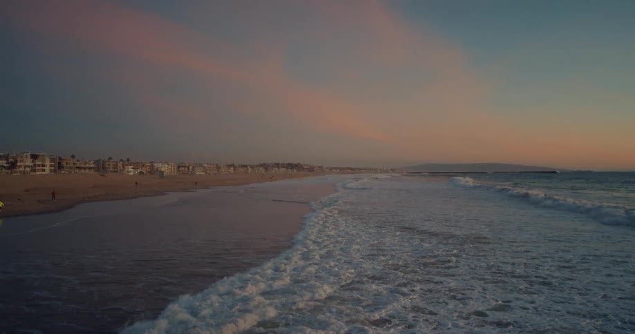 Ocean waves break against the long beach at dusk