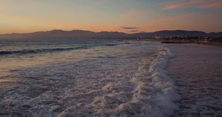 Waves are slowly crashing on shore near a mountain range