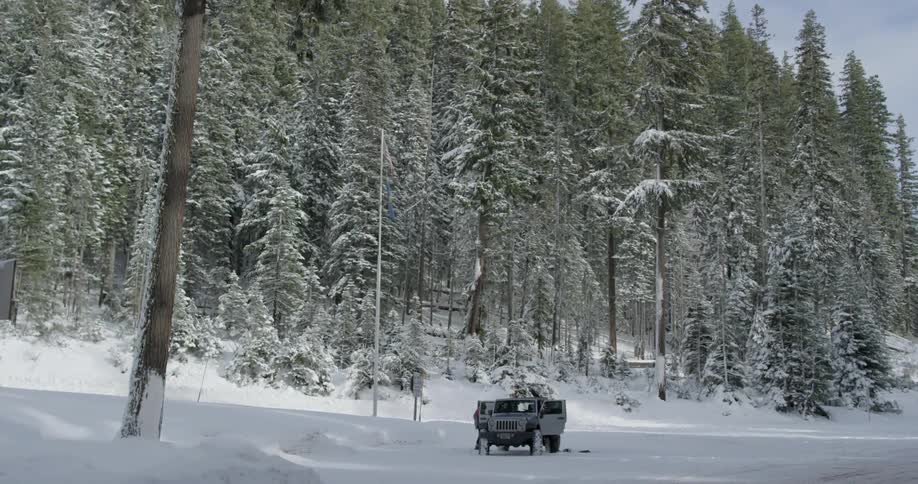 Two people are near a vehicle in the snow