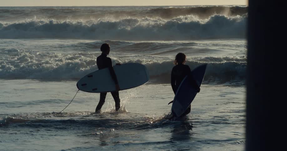 Man and woman are surfing on the ocean at dusk