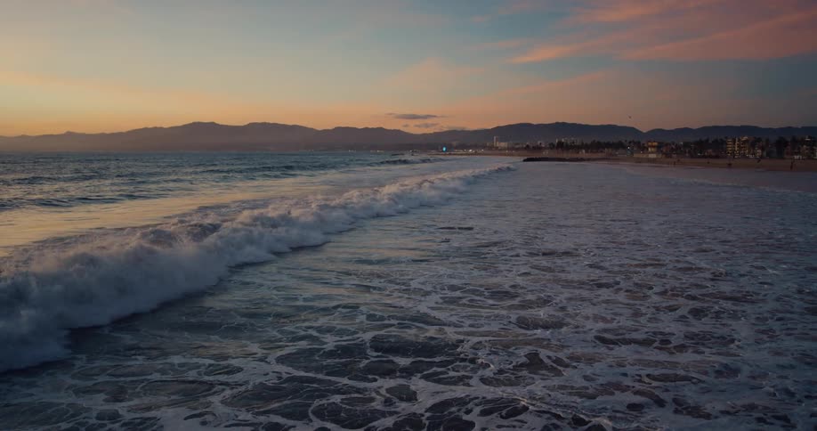 Waves rolling over a beach with buildings along the coast and mountains on the horizon