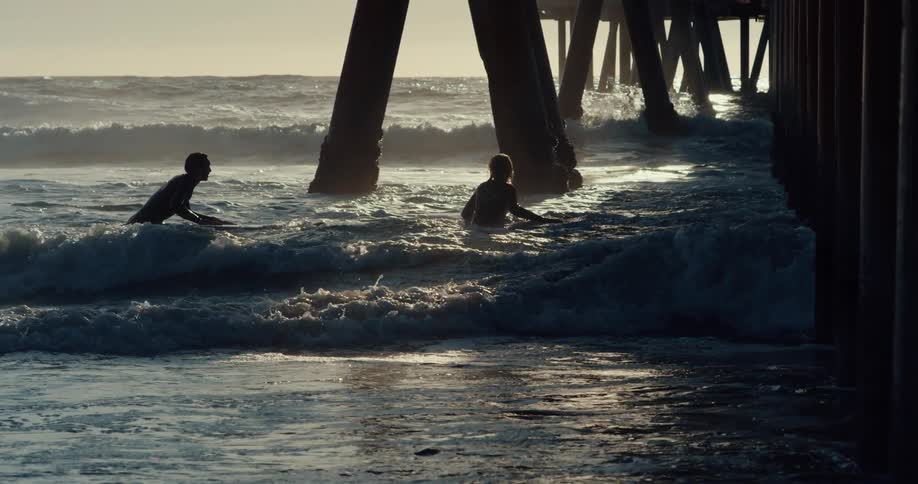Two men are in the ocean surfing at dusk