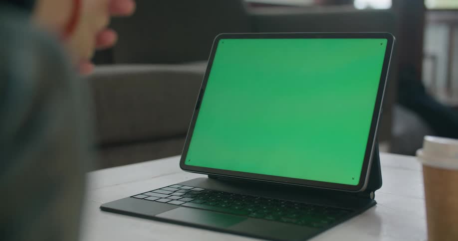 A person sits in front of a laptop with a green screen