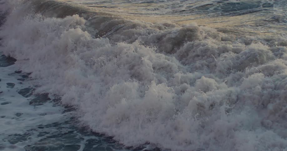 Ocean wave breaks against the shore at dusk