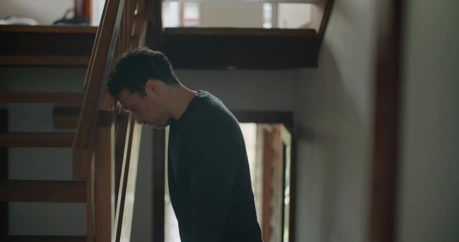 A man leans his head on a stair rail in a dark room