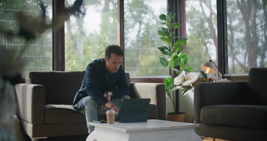 Man with a blue shirt and jeans uses a tablet on a marble table in the living room at home