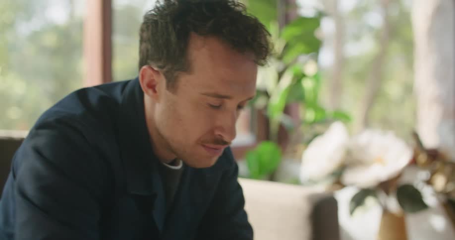 A man is sitting on a couch and typing on a laptop