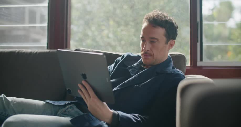 Man resting on a couch at home typing on a tablet
