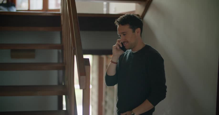 A man speaks on his smartphone while standing in the middle of a staircase in a house during the day