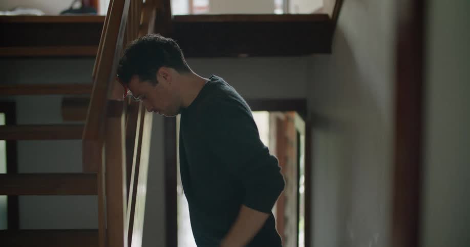 Man with dark sweater leans his head against the stairs while using smartphone