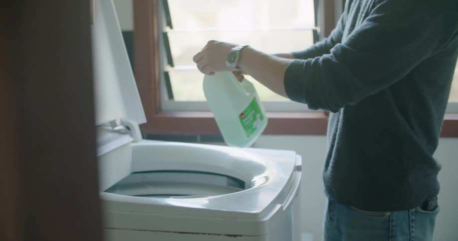 Man adds laundry detergent and clothes to washing machine before starting cycle