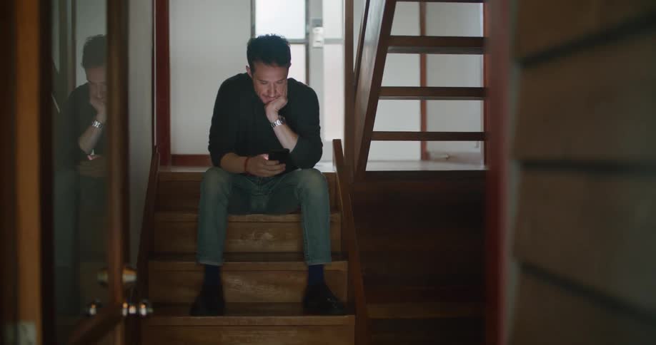 A man sitting on a staircase using a smart phone with a wall in the background