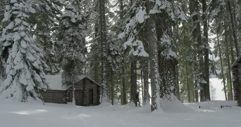 Two women wearing snowshoes hike away from a cabin in a snow-covered landscape