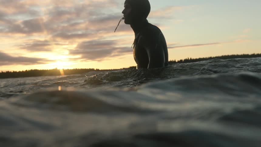 A man is standing in the water at sunset