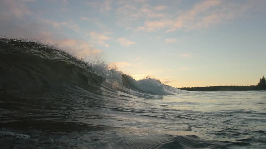 A wave rolls and breaks to a curl at sunset