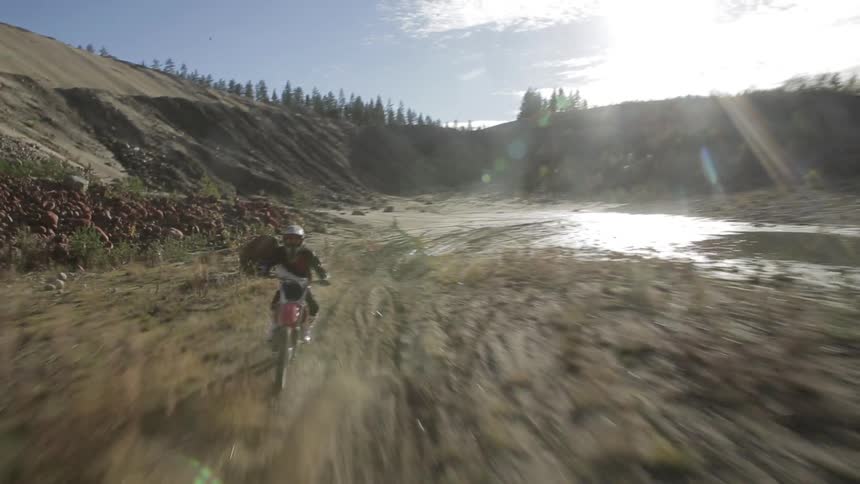 A person rides a dirt bike through a dirt and rock-covered area