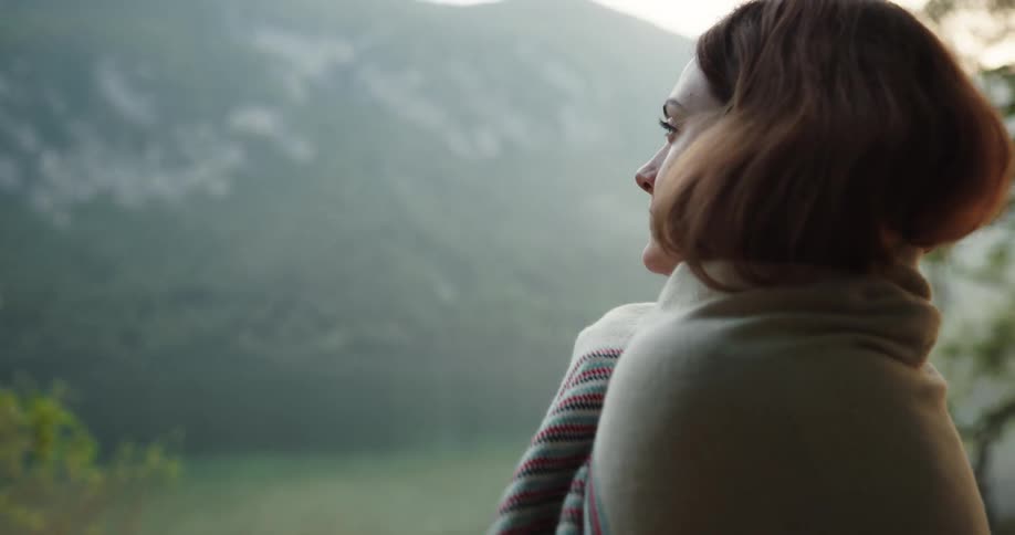 A woman is putting on a coat and standing outdoors