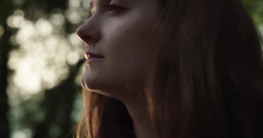 Woman with brown hair drinks out of copper cup and looks around at sunset in the forest